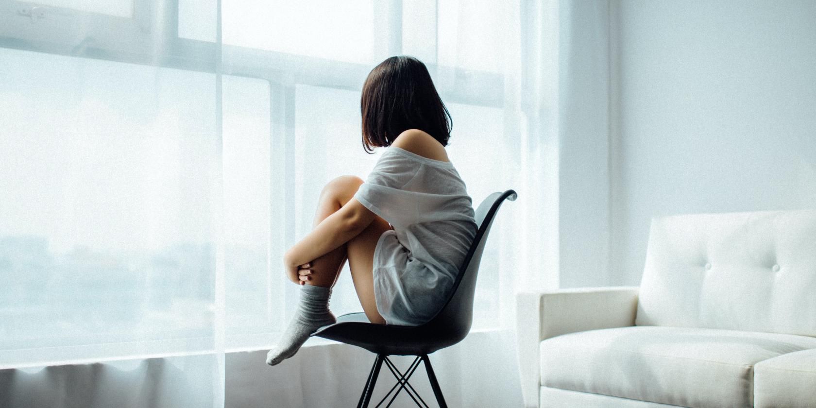 Gadis kesepian duduk di kursi sendirian di ruangan putih yang menggambarkan depresi