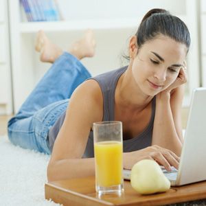 Happy woman lying on floor at home and working on laptop