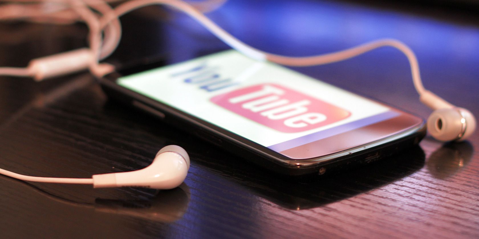 Phone on table showing the YouTube logo, with earbuds connected