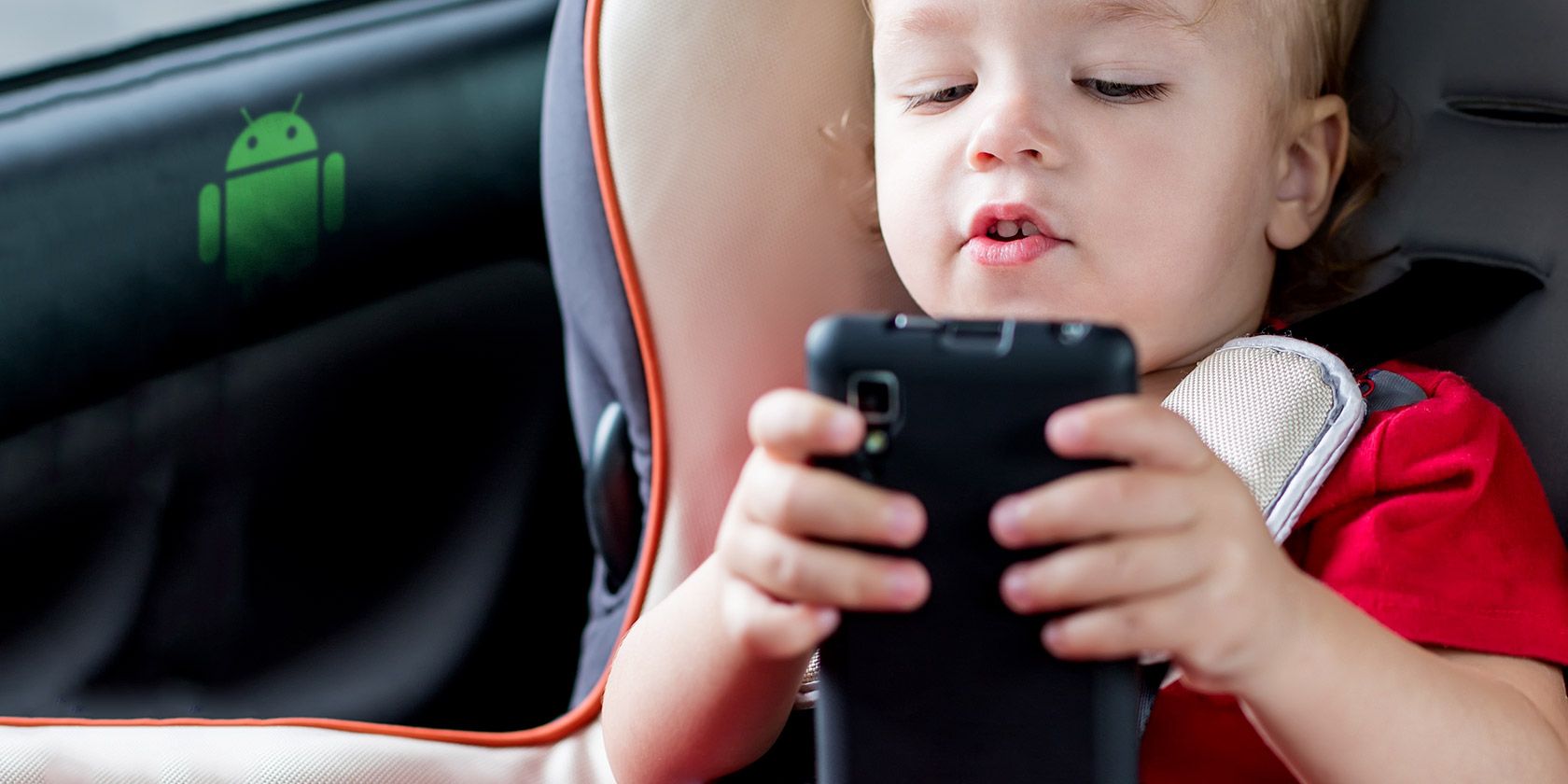 Young child using a smartphone in a car seat.
