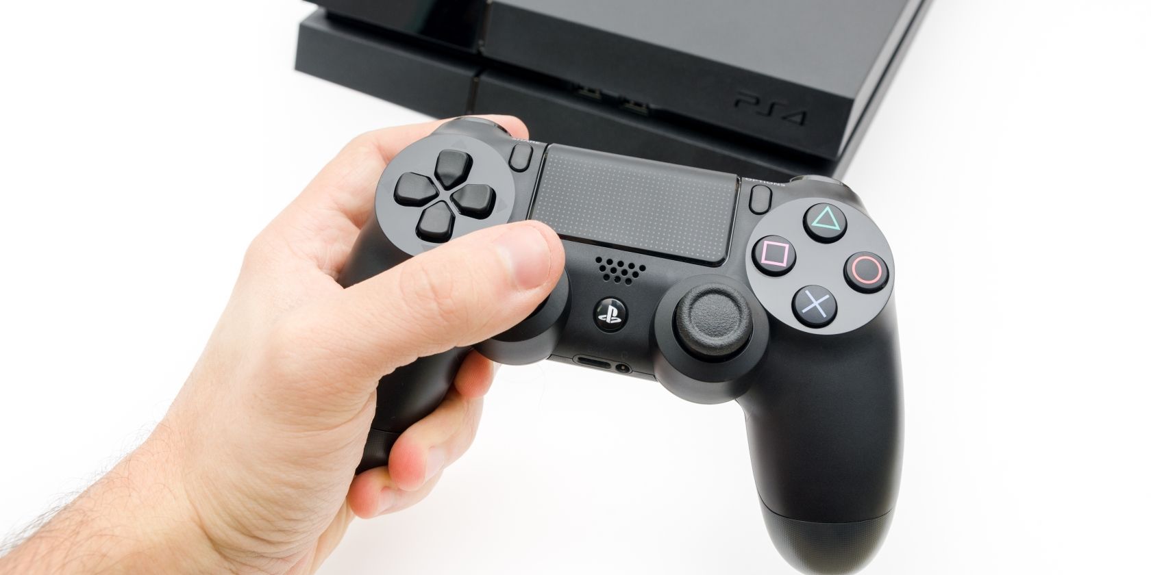 Hand holding PS4 controller in front of PS4 console