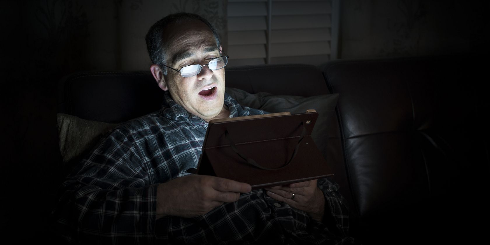 Man reading computer tablet in the dark with its bright light shining in his face