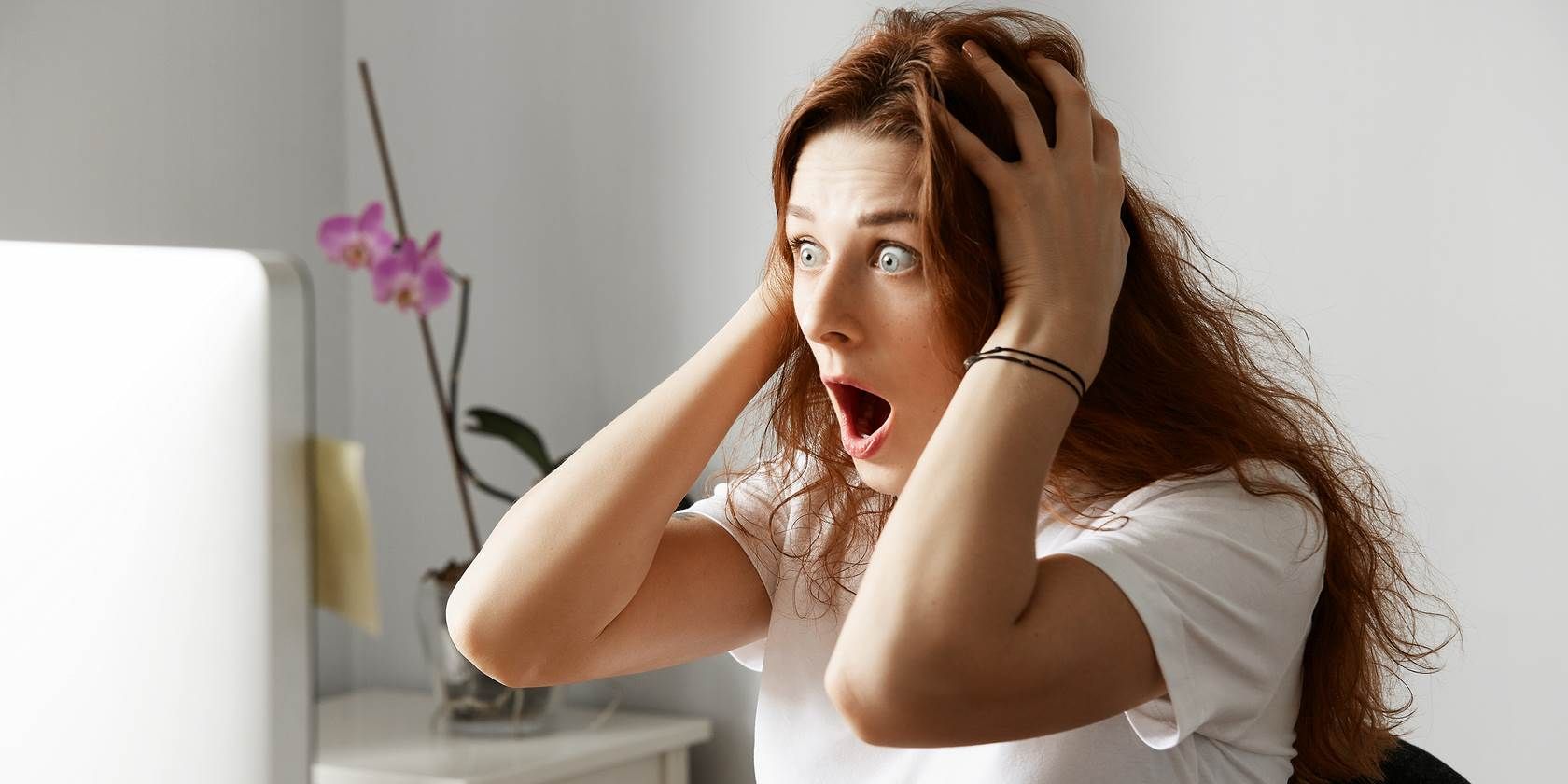 Woman grasping her head in shock while looking at a PC