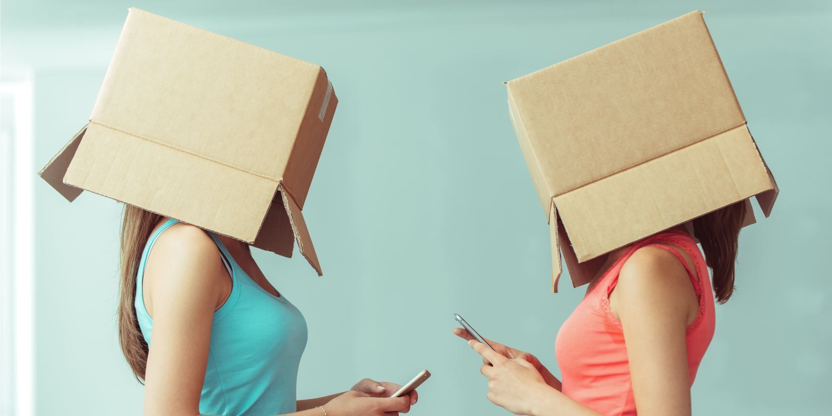 Two women with cardboard boxes on their heads using smartphones 