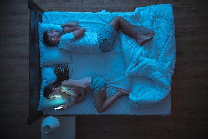 wife using smartphone in bed while husband sleeps