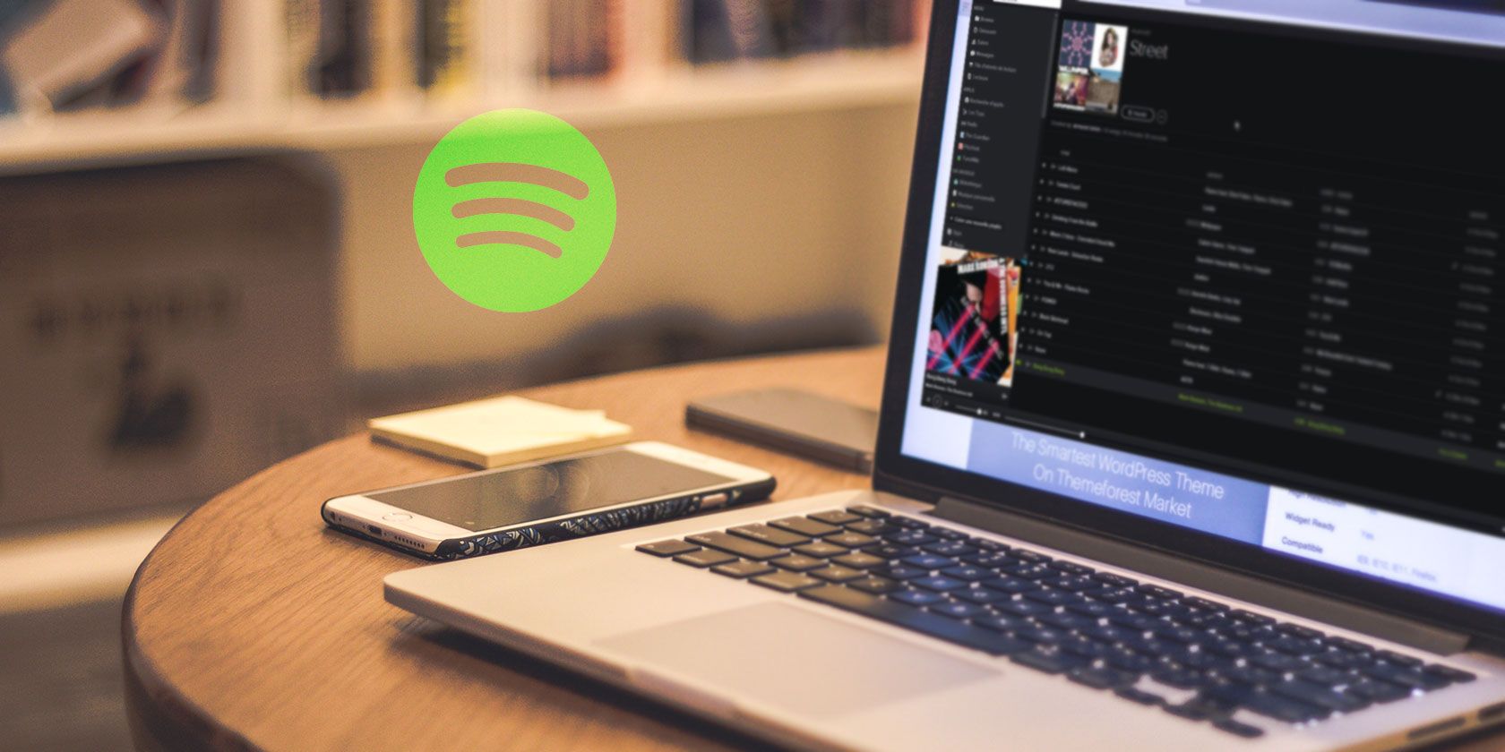 Spotify logo next to laptop on a table showing Spotify app