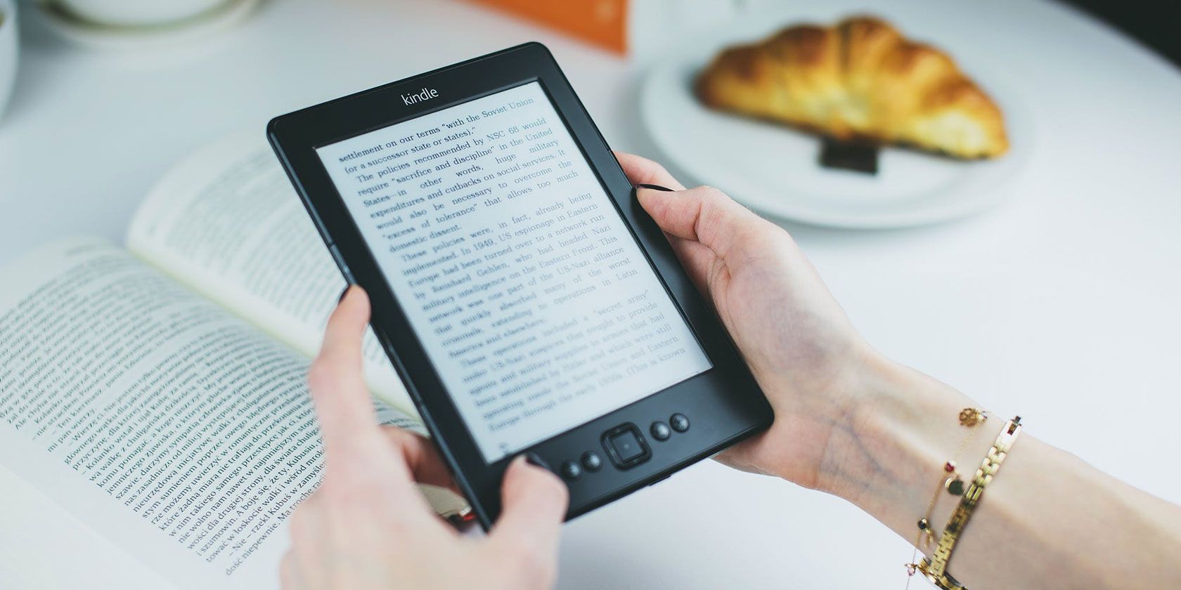 Hands holding an old Kindle model and reading a book