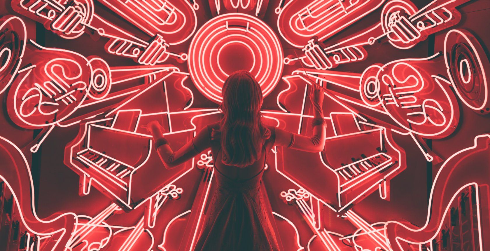 a lady standing like a composer in front of a wall of musicla instrument shaped neon lights