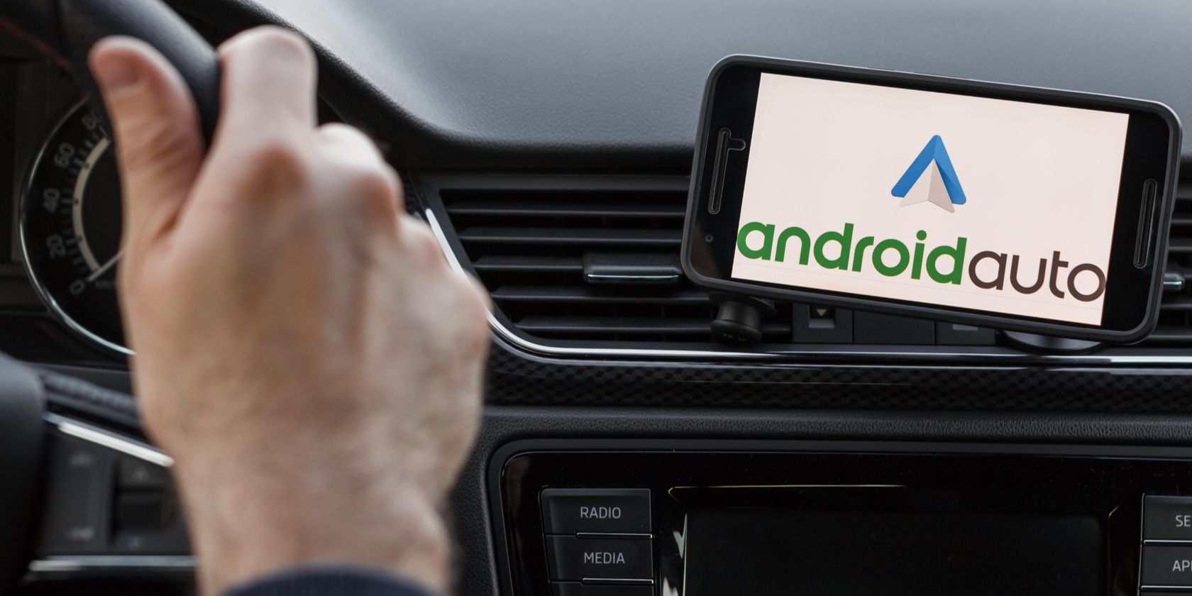 Hands on steering wheel with phone showing Android Auto logo