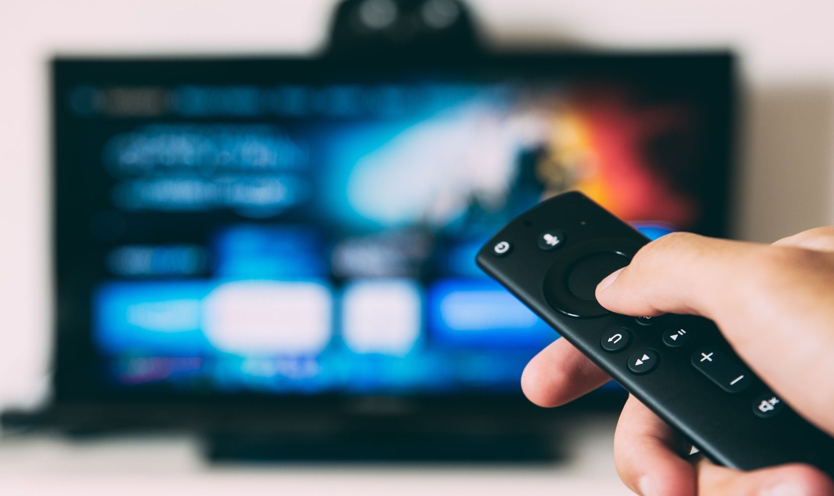 Person Holding Remote With Television In Background - NanoCell vs. OLED: quale tecnologia TV dovresti scegliere?