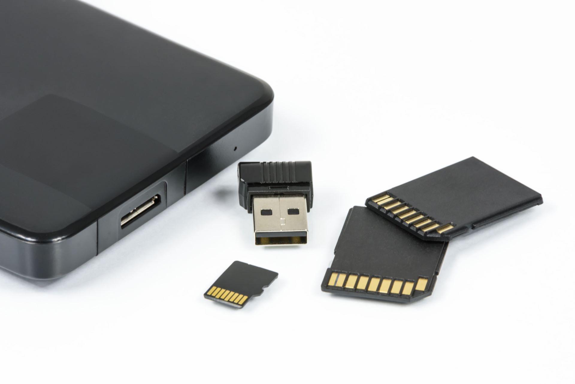 Black external hard drive, usb stick, and flash cards on a white surface