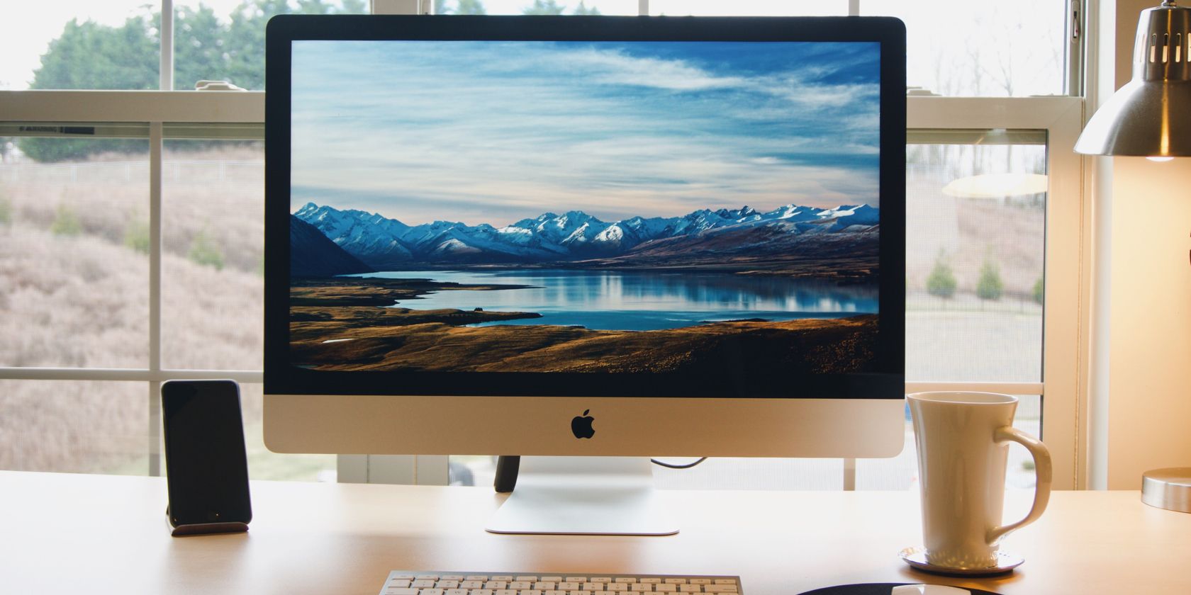 A photograph of an iMac sitting in front of a window framing a picturesque scene