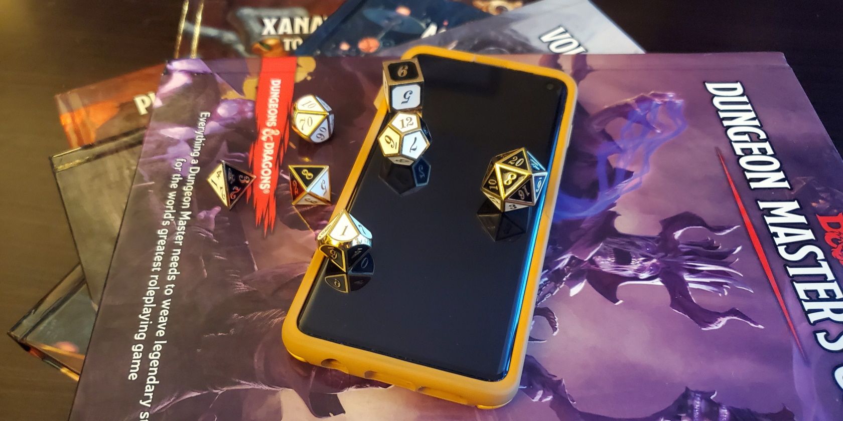 an android phone sits on top of some dungeons and dragons rulebooks, with a set of polyhedral dice scattered over it.
