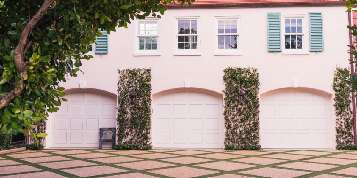 Pink house with three garage doors and green hedges