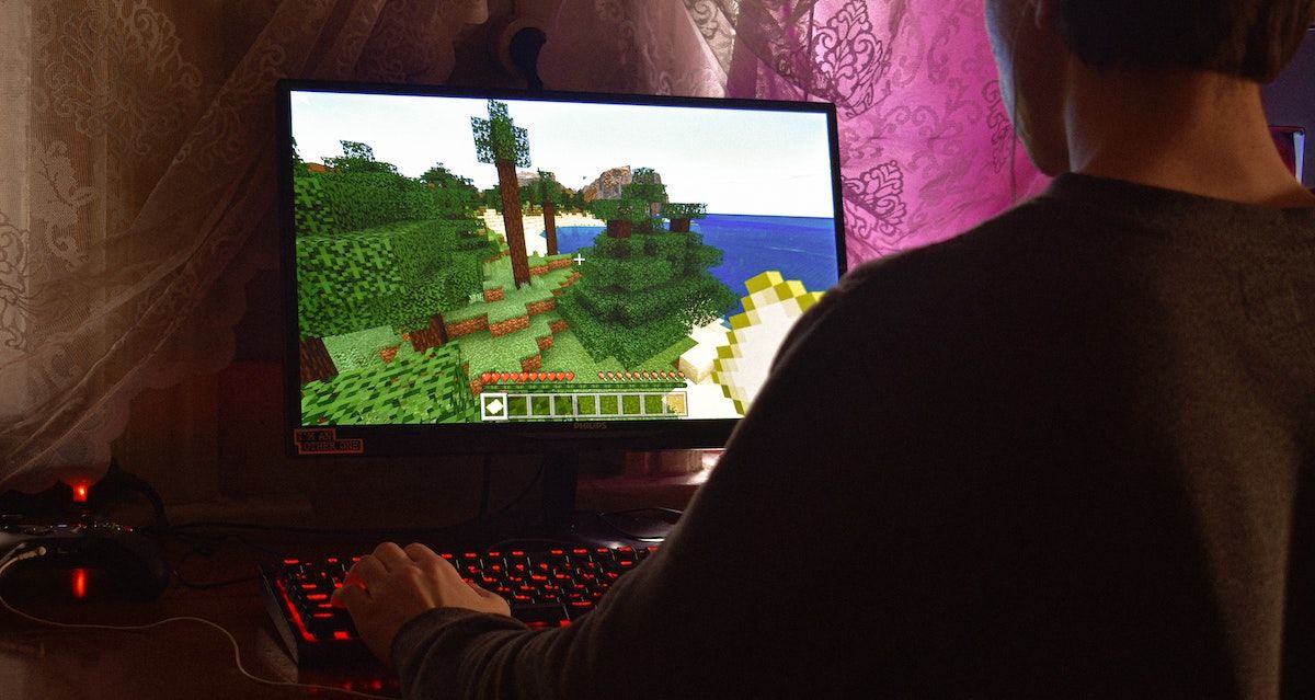 A person playing Minecraft on a computer with a keyboard with glowing red accents