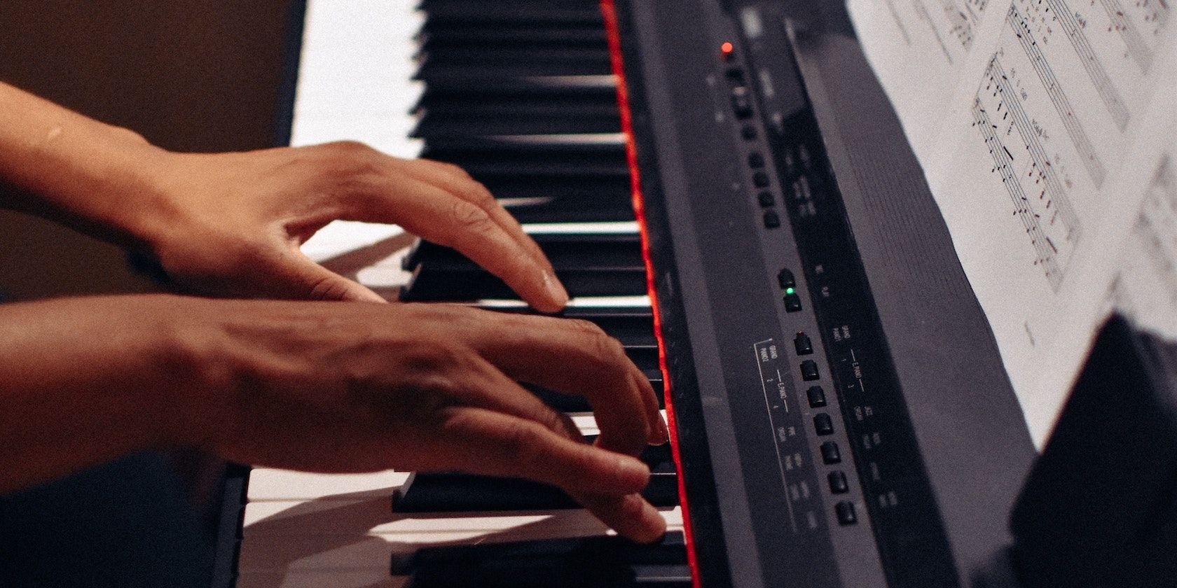 A person playing a keyboard with both hands and with sheet music and a red light and green light on.