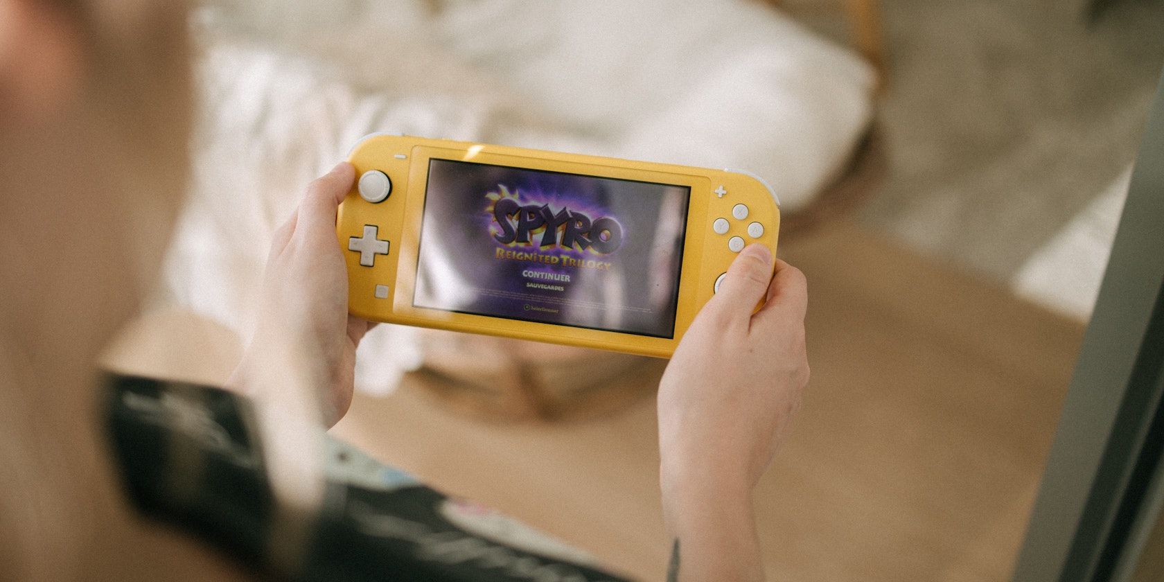 A photograph showing somebody holding a yellow Nintendo Switch Lite with the game Spyro Reignited Trilogy on screen