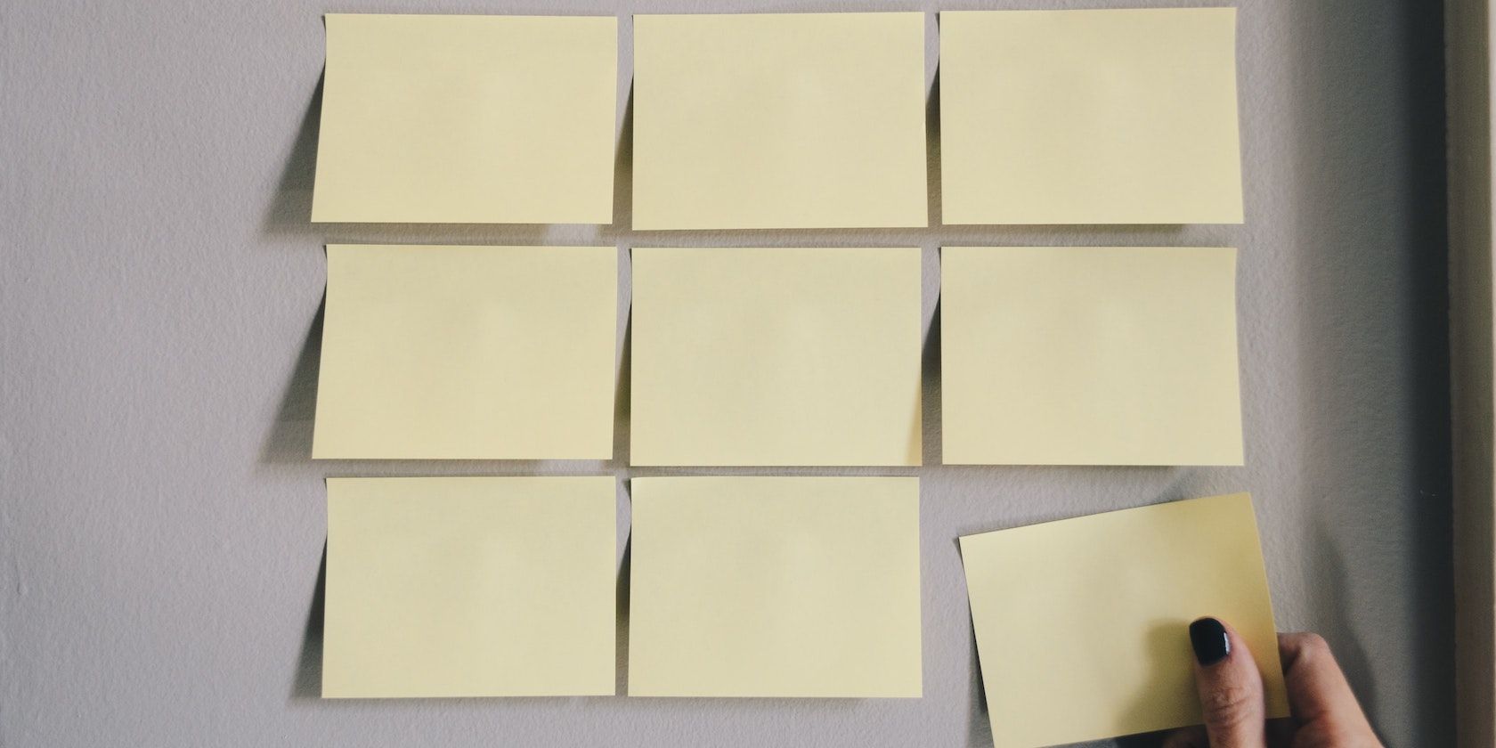 A grid of yellow sticky notes with a hand removing the lower right note