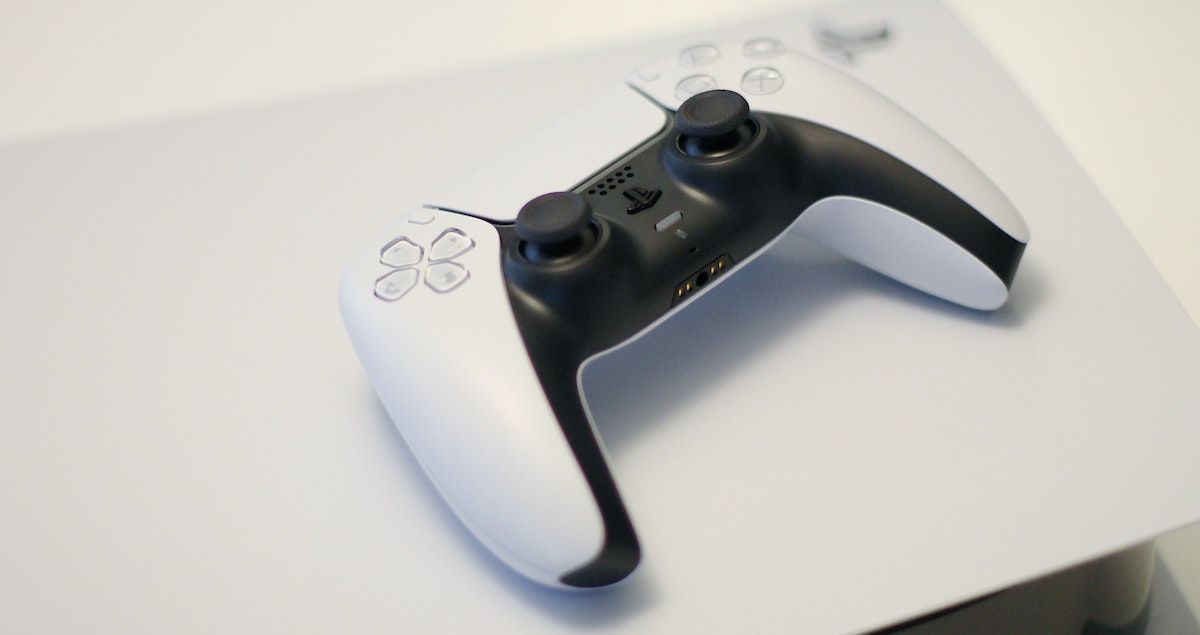 A PS5 DualSense controller against a PS5 console that is blurred