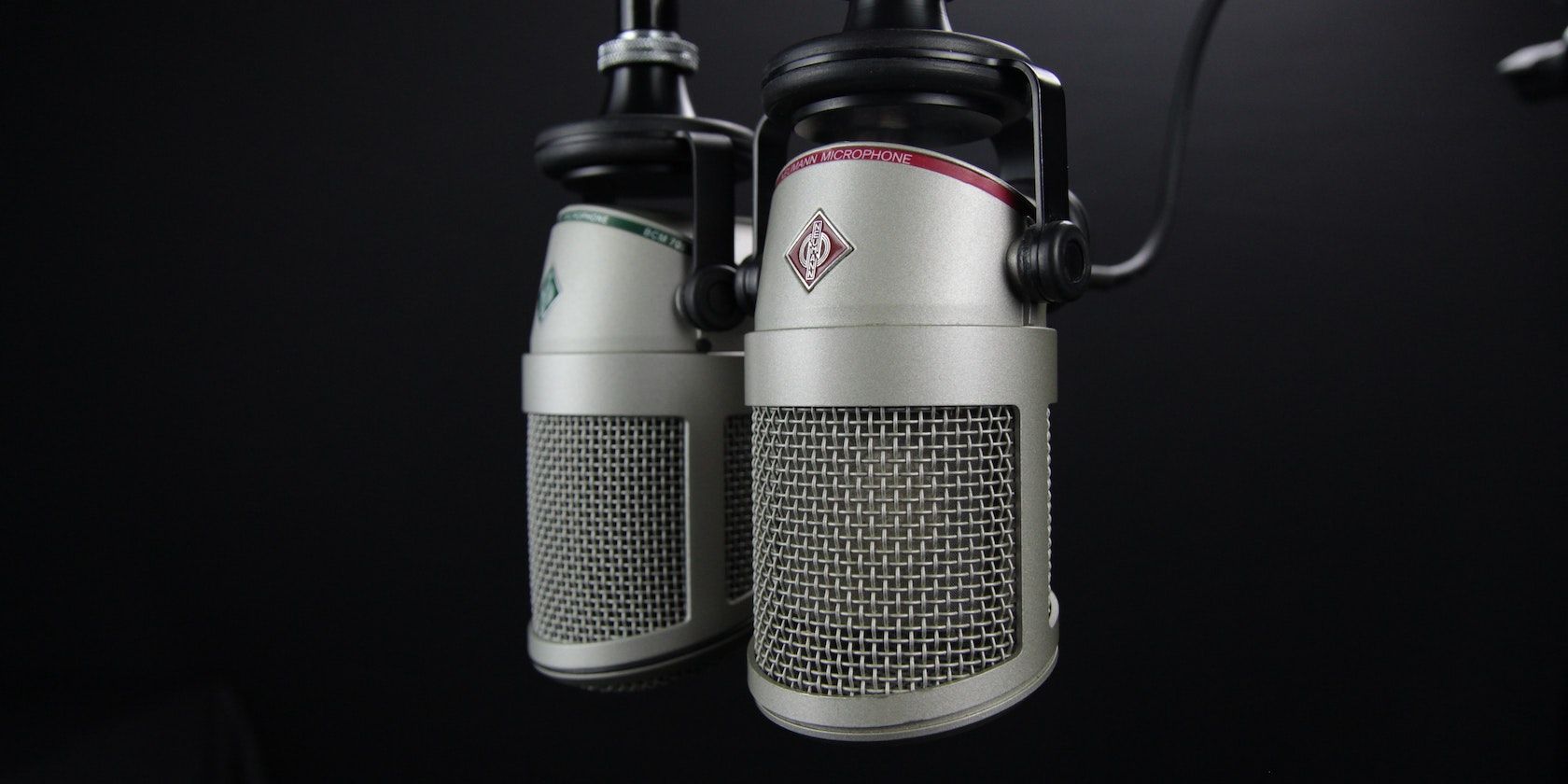 Two gray condenser microphones side by side with a black background