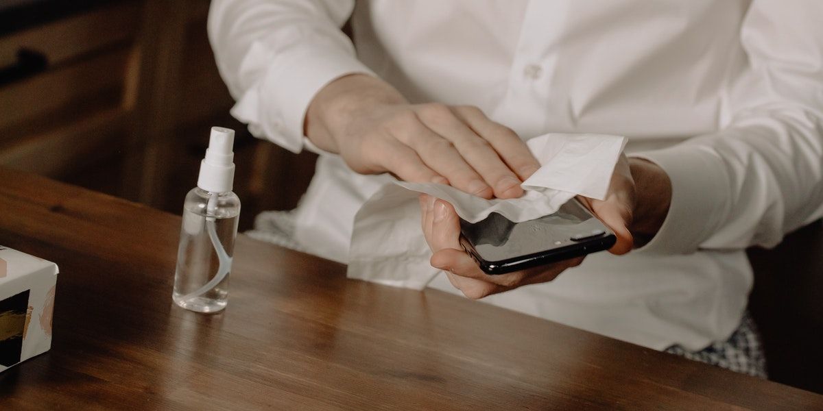 Cleaning Phone while Wearing Dress Shirt at Wooden Table