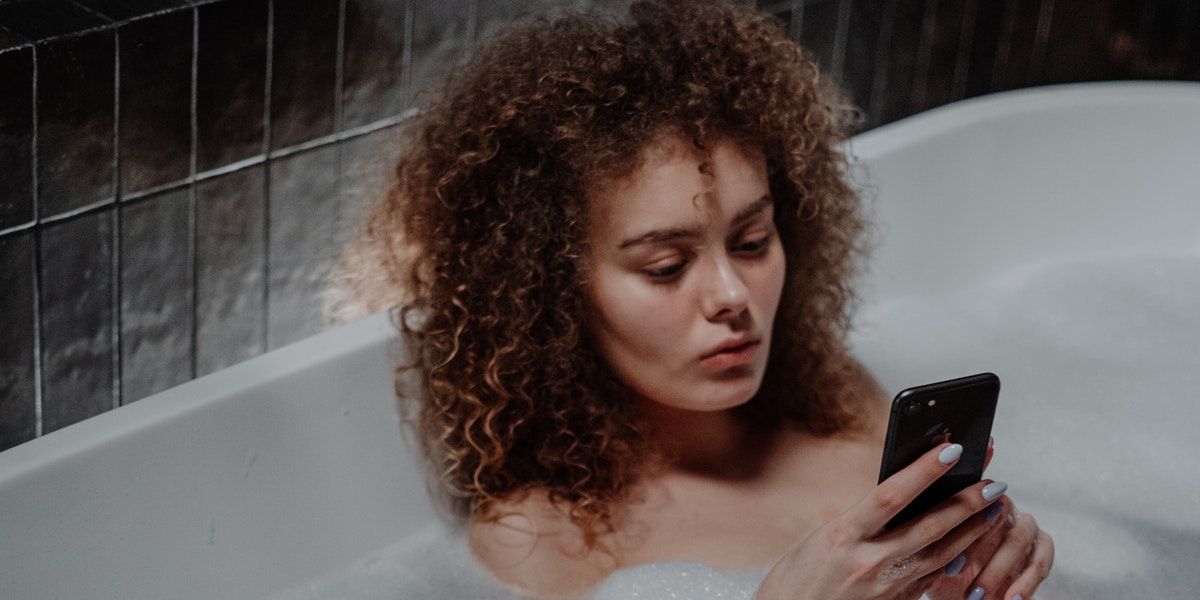 Woman sitting in bubblebath using phone