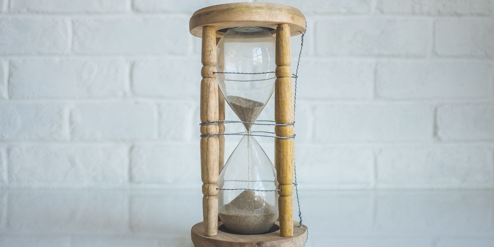 A photograph of an hourglass showing sand trickling through a tiny hole from one glass bowl into another below it