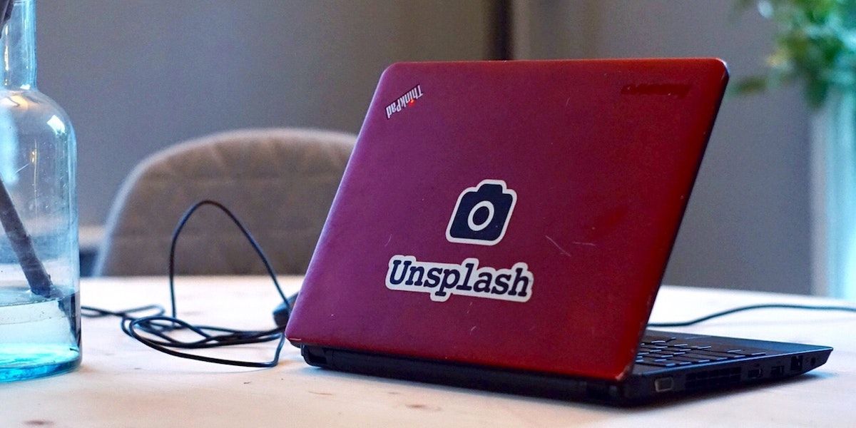 A laptop charging with a red case with the Unsplash logo on top.
