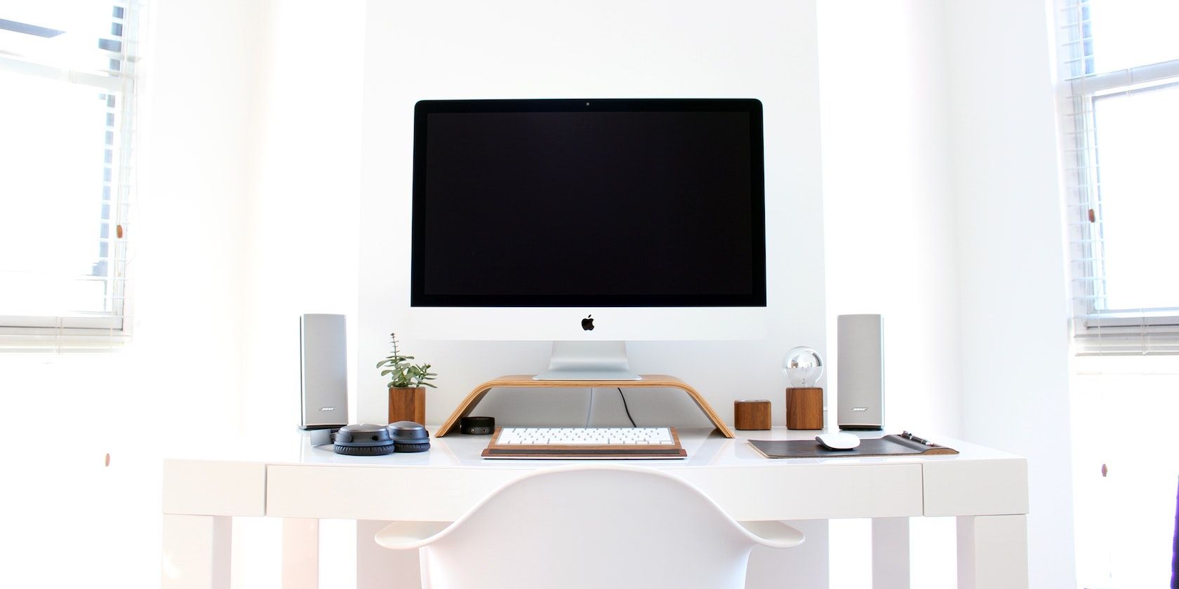 A photograph of a desktop iMac on an organised desk, in a white room with white furniture