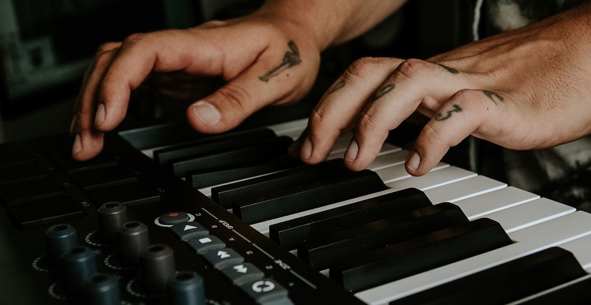 Person playing a synthesizer with finger tattoos.
