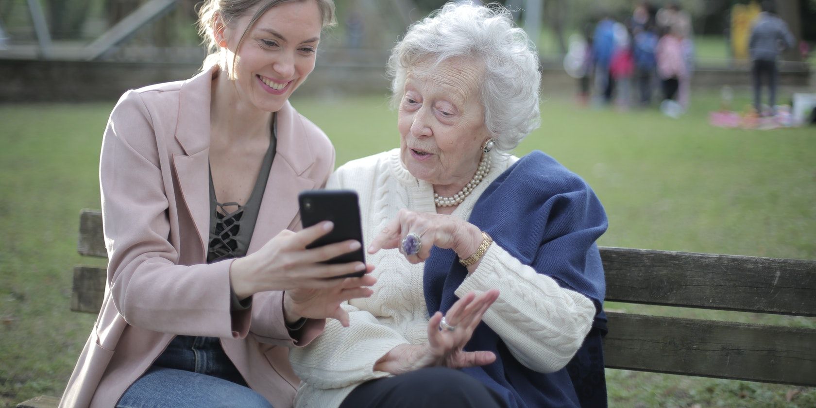 Two women, one young and one old, using a cell phone on a park bench.