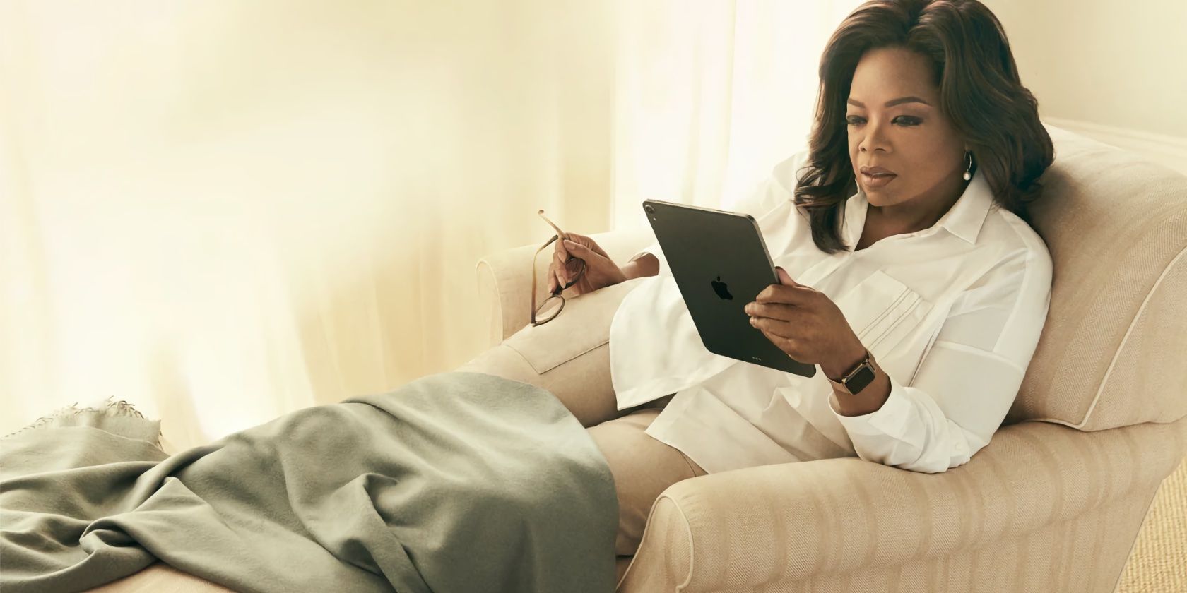 A promotional photograph showing Oprah laying on her crouch and reading a book on her iPad