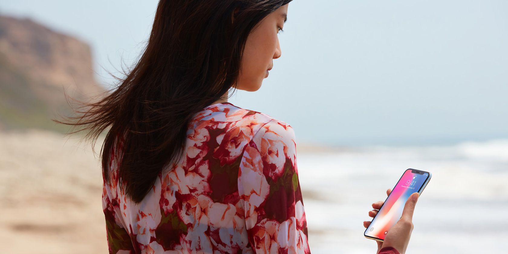 A young woman standing at the beach and unlocking her iPhone X with Face ID