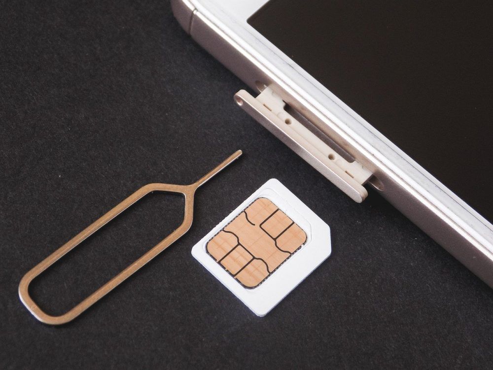 A SIM card and ejector, next to an iPhone.