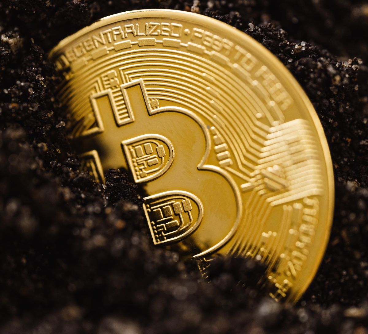 A golden coin with Bitcoin's symbol on it among the dirt.