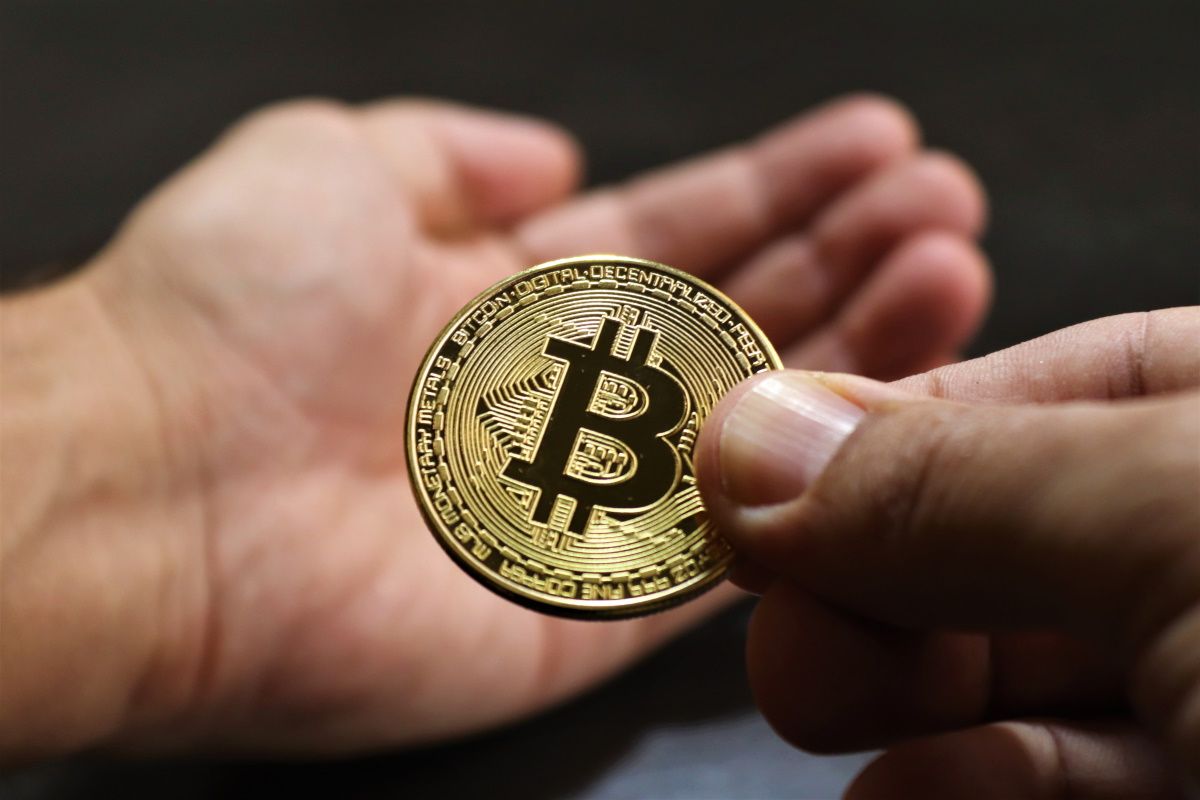 A hand giving a golden coin with Bitcoin's symbol on it to other hand