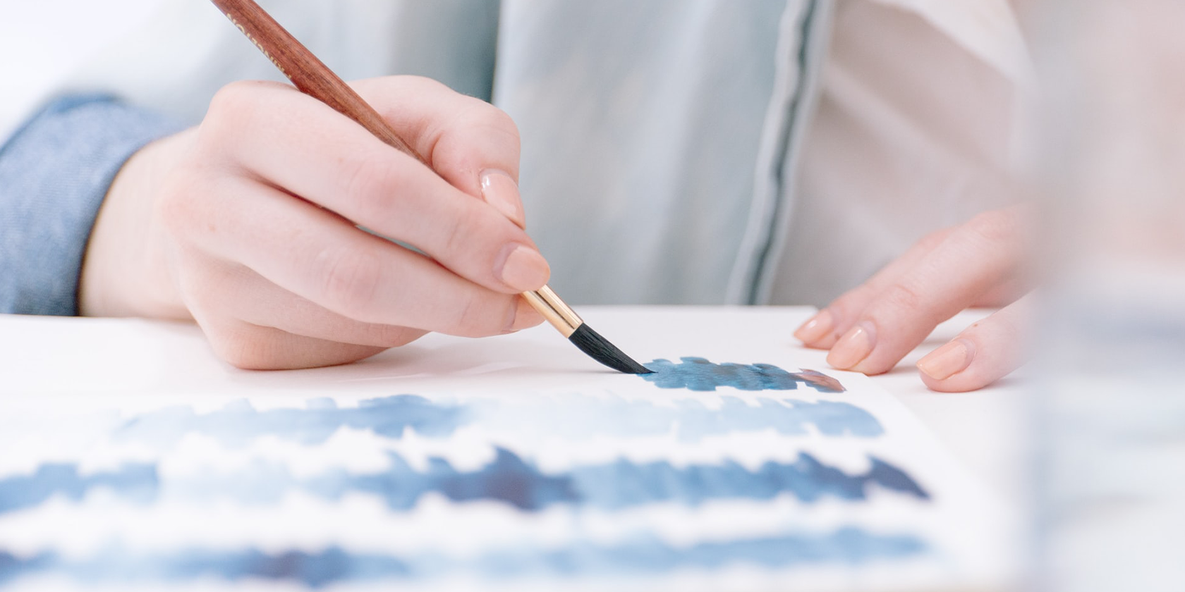 An artist strokes with blue watercolor paints