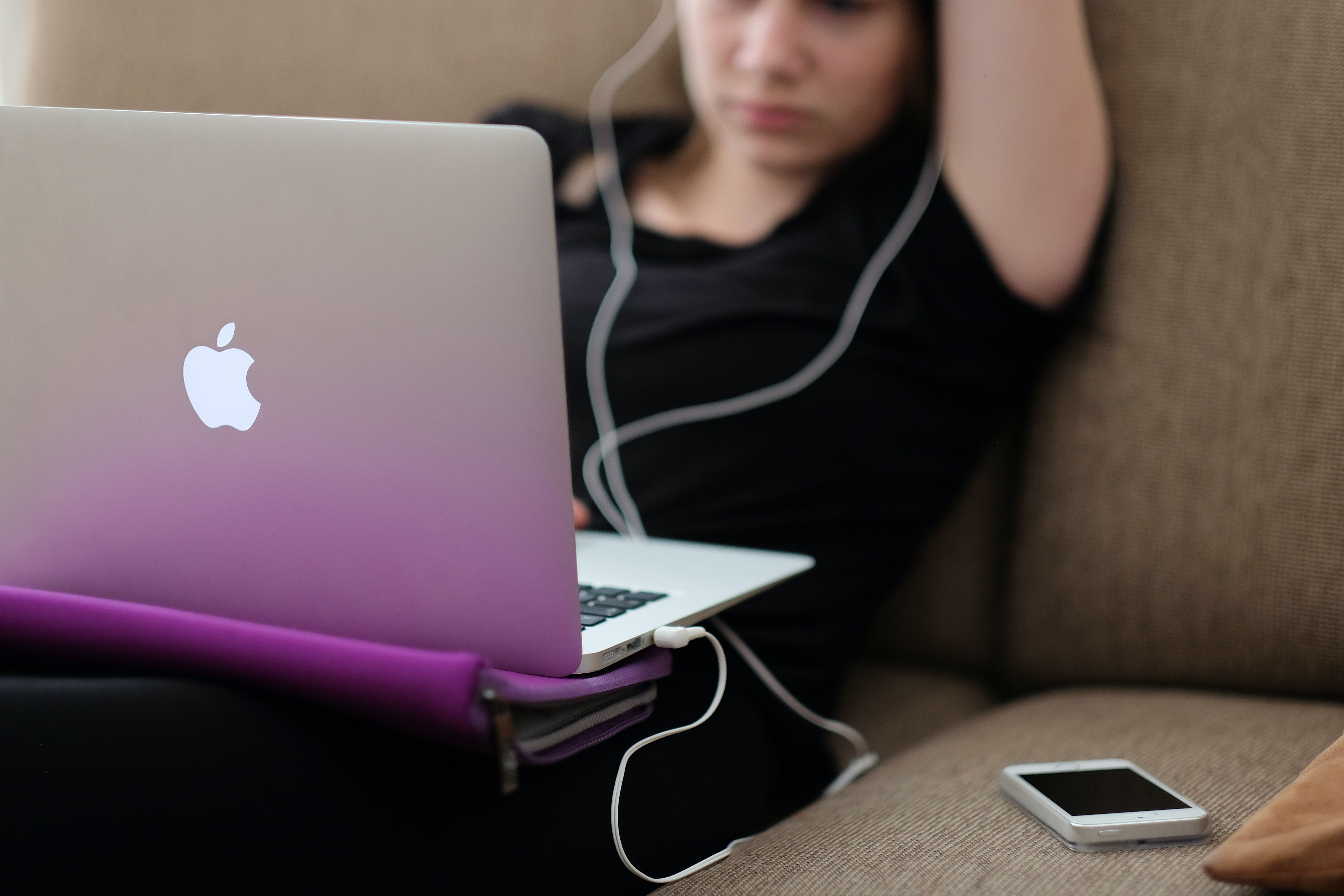 A person wearing a simple earbuds headset uses a Macbook.
