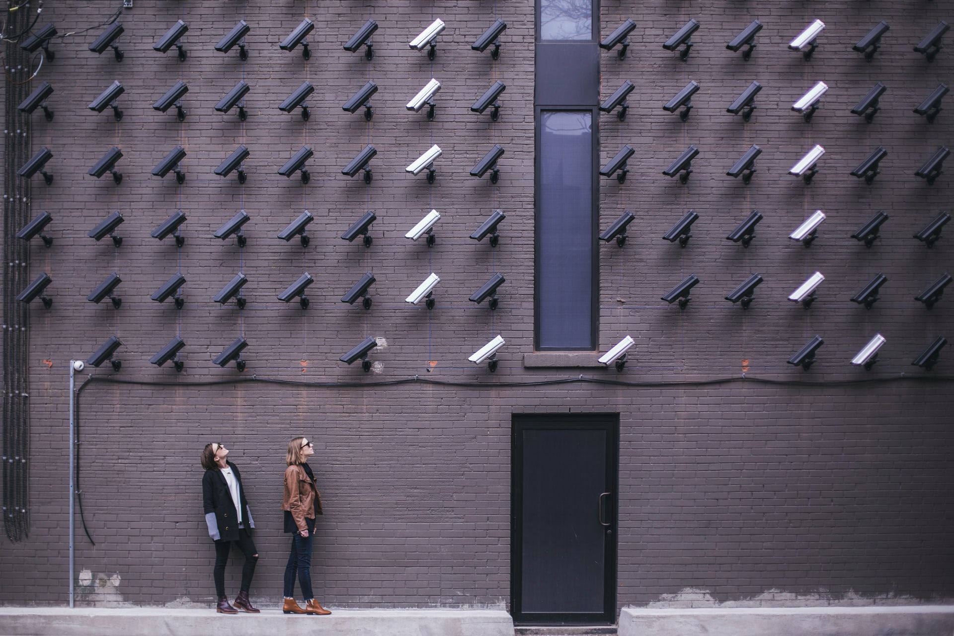 A wall of security cameras and two people looking at them