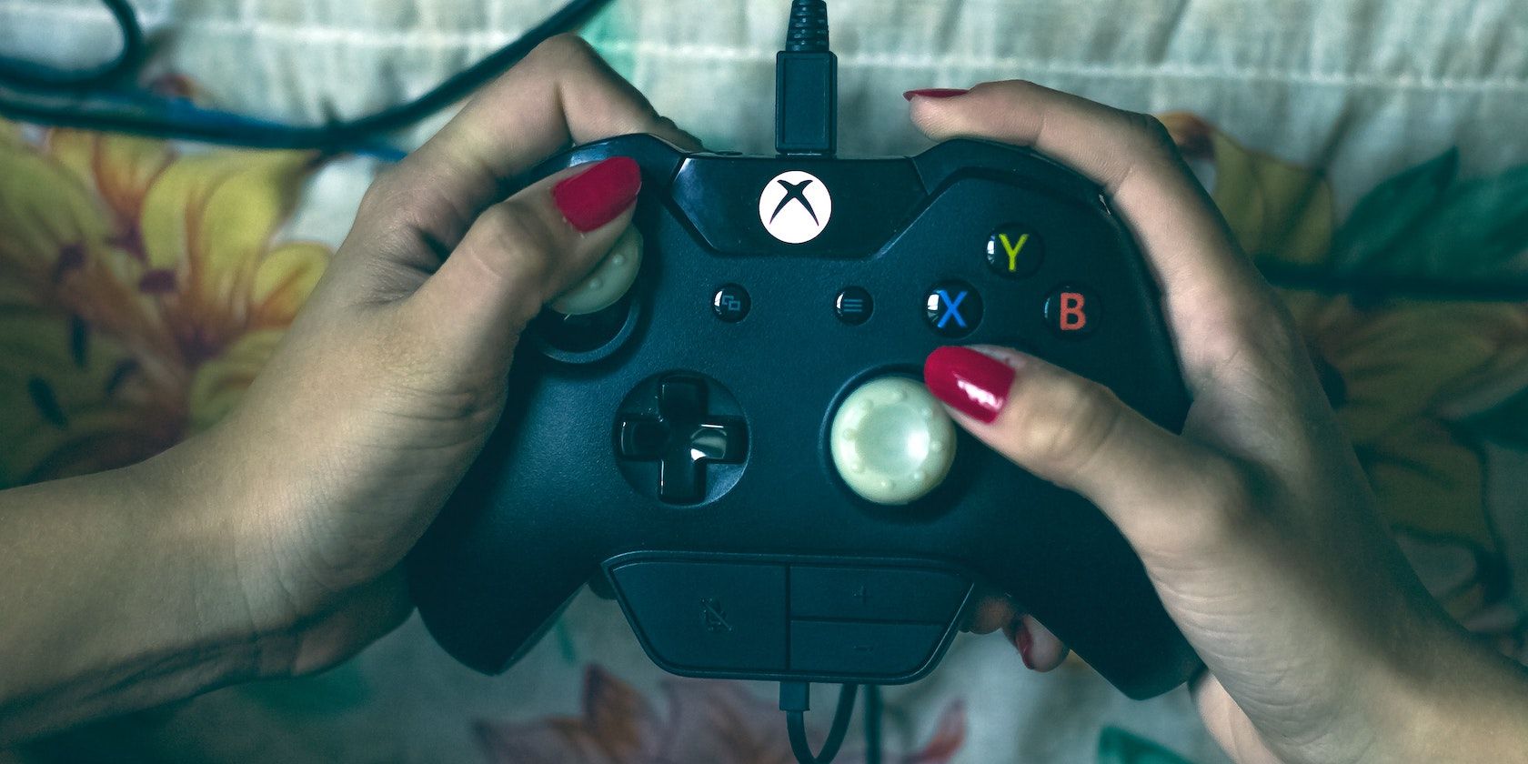 An Xbox One controller is held by two hands with painted nails.