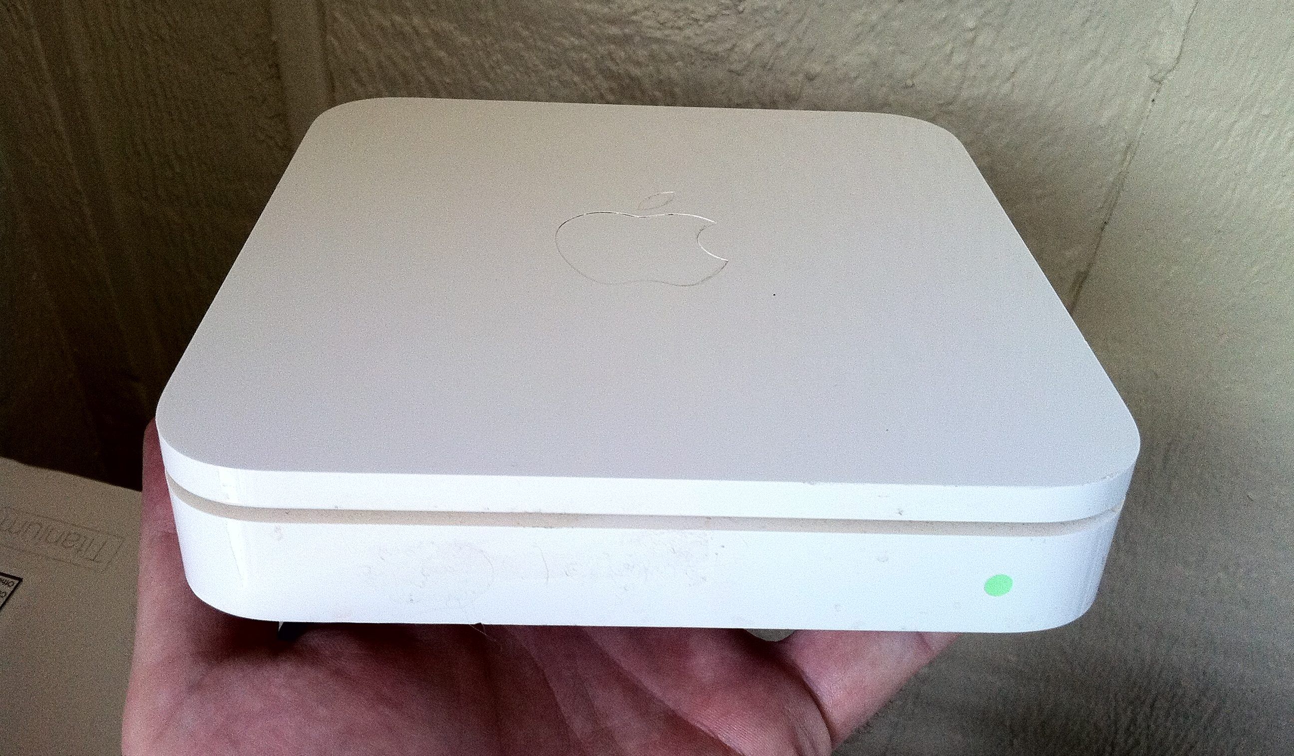 The square model of an AirPort Extreme is held up by a hand