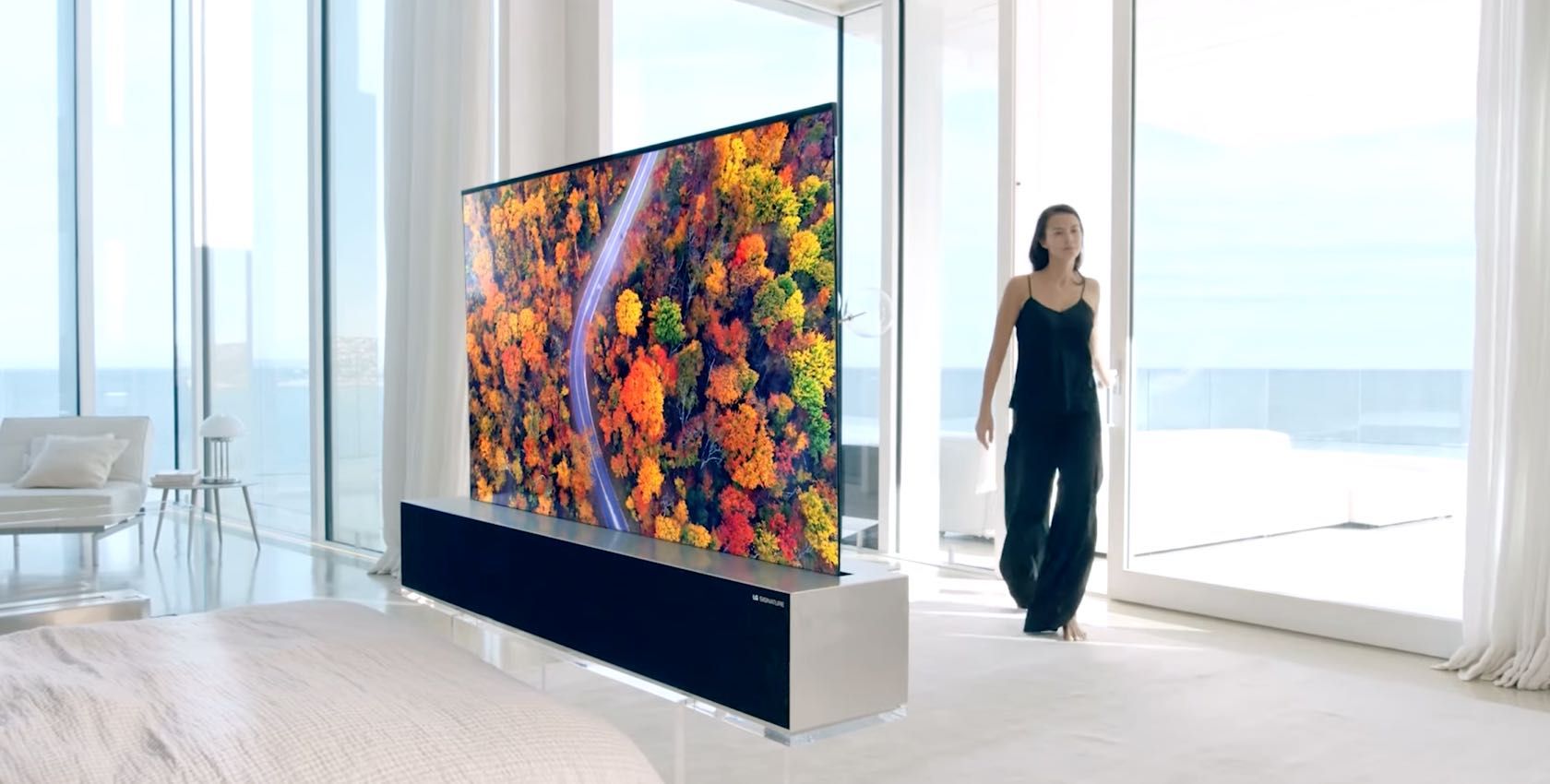 A still from an LG ad for its Signature rollable OLED TV showing a young woman in a luxury home with the rollable TV installed