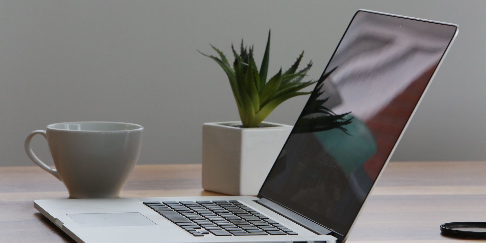 A MacBook sits on a table beside a plant and a mug