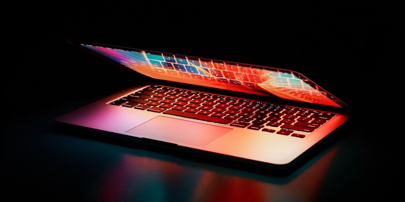 A partially open MacBook sits on a table in the dark