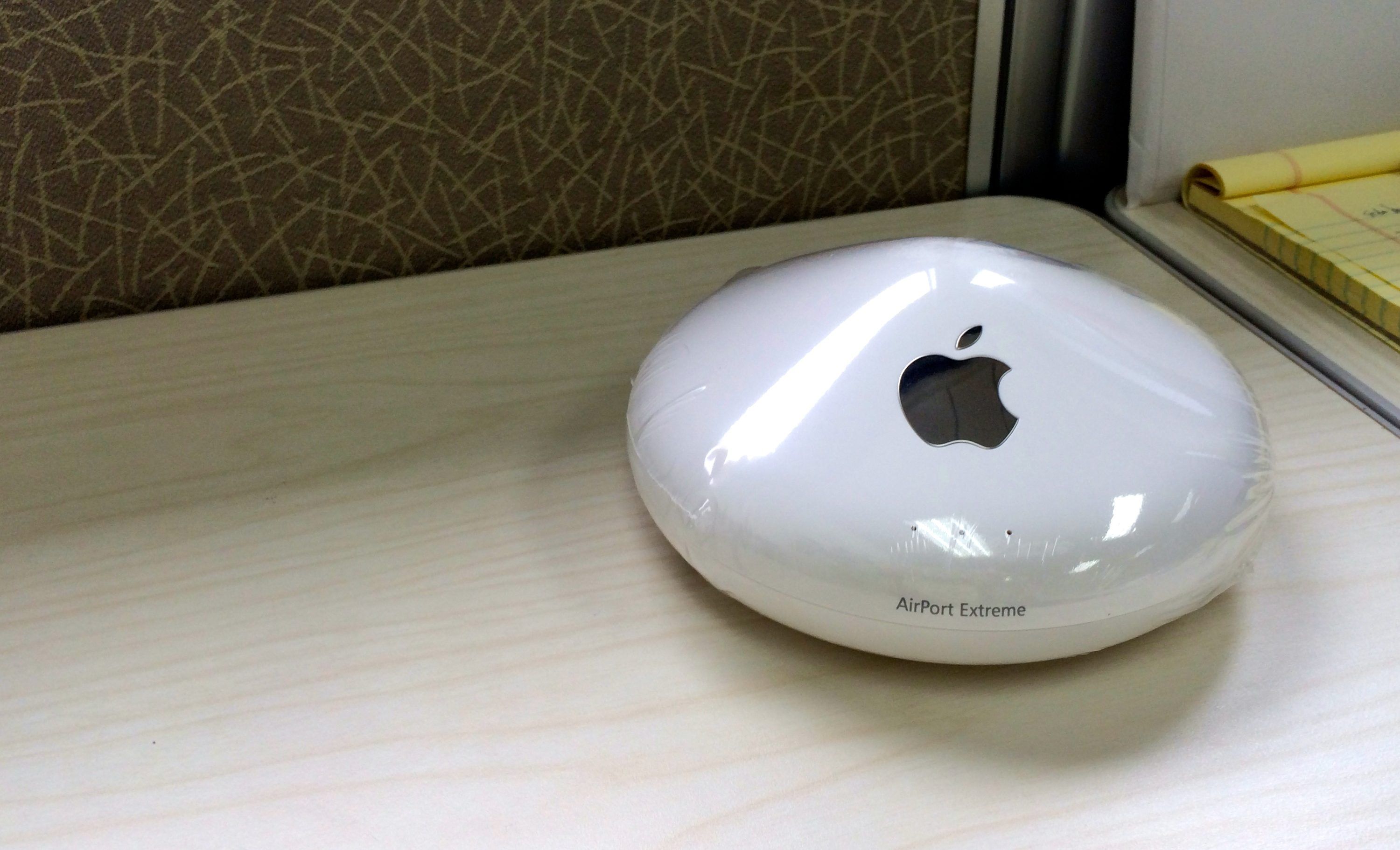 The round, original model of the AirPort Extreme router sits on a table near a wall