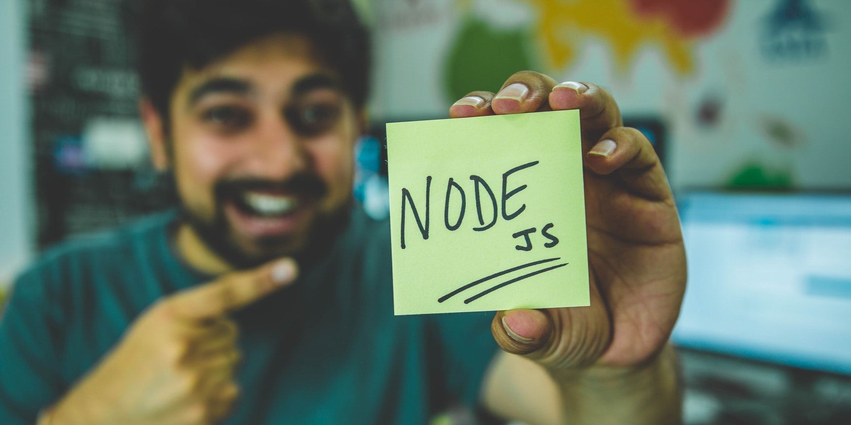 Man holding up a yellow square of card with “Node.js” written on it.