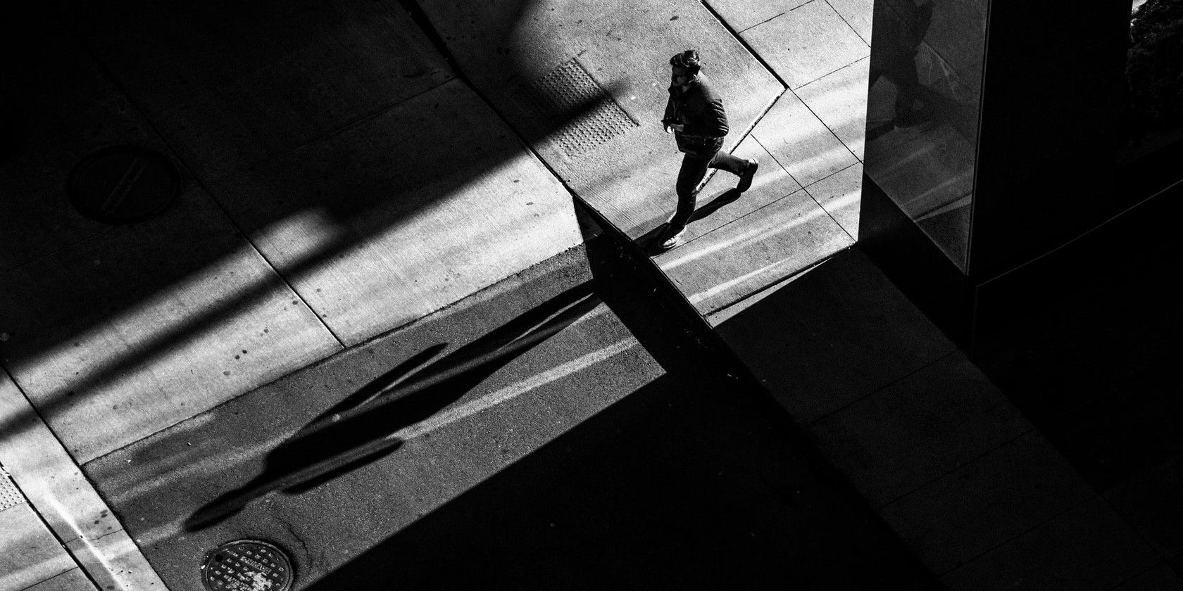 Man Crossing Street and Casting a Long Shadow in Monochrome
