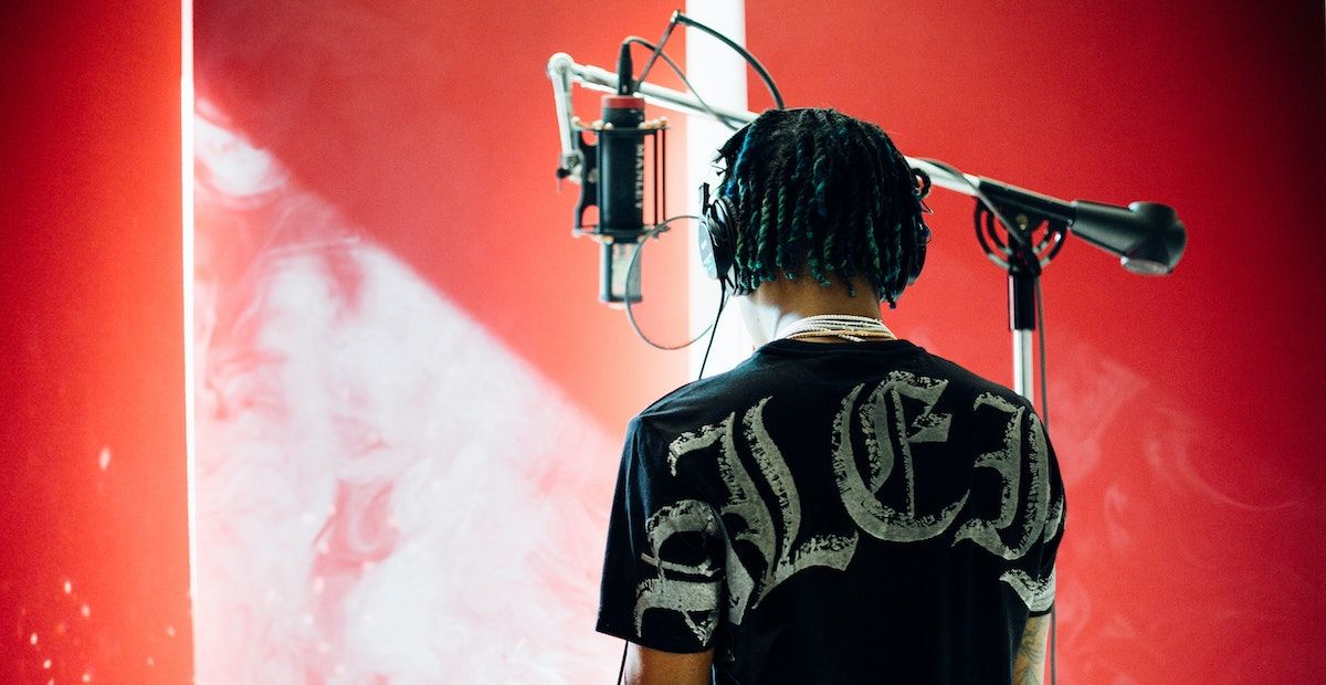 A person standing in front of a microphone with their back to the camera and a red wall in the background.