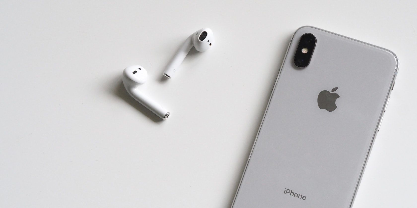 AirPods lying next to an iPhone on a white surface.