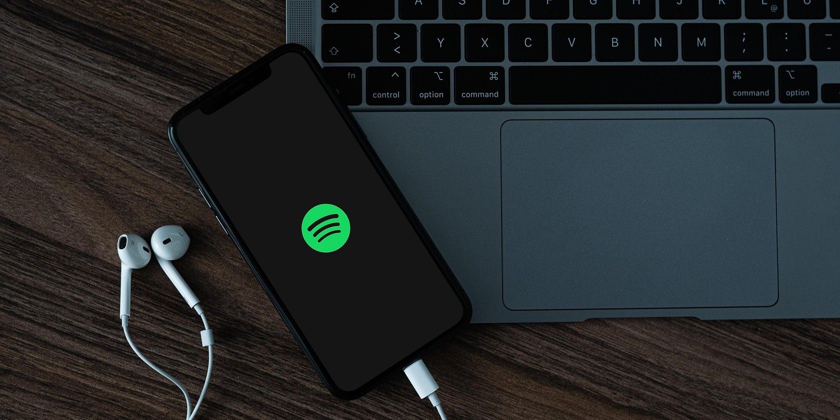 spotify logo on iphone next to a macbook air with headphones plugged in